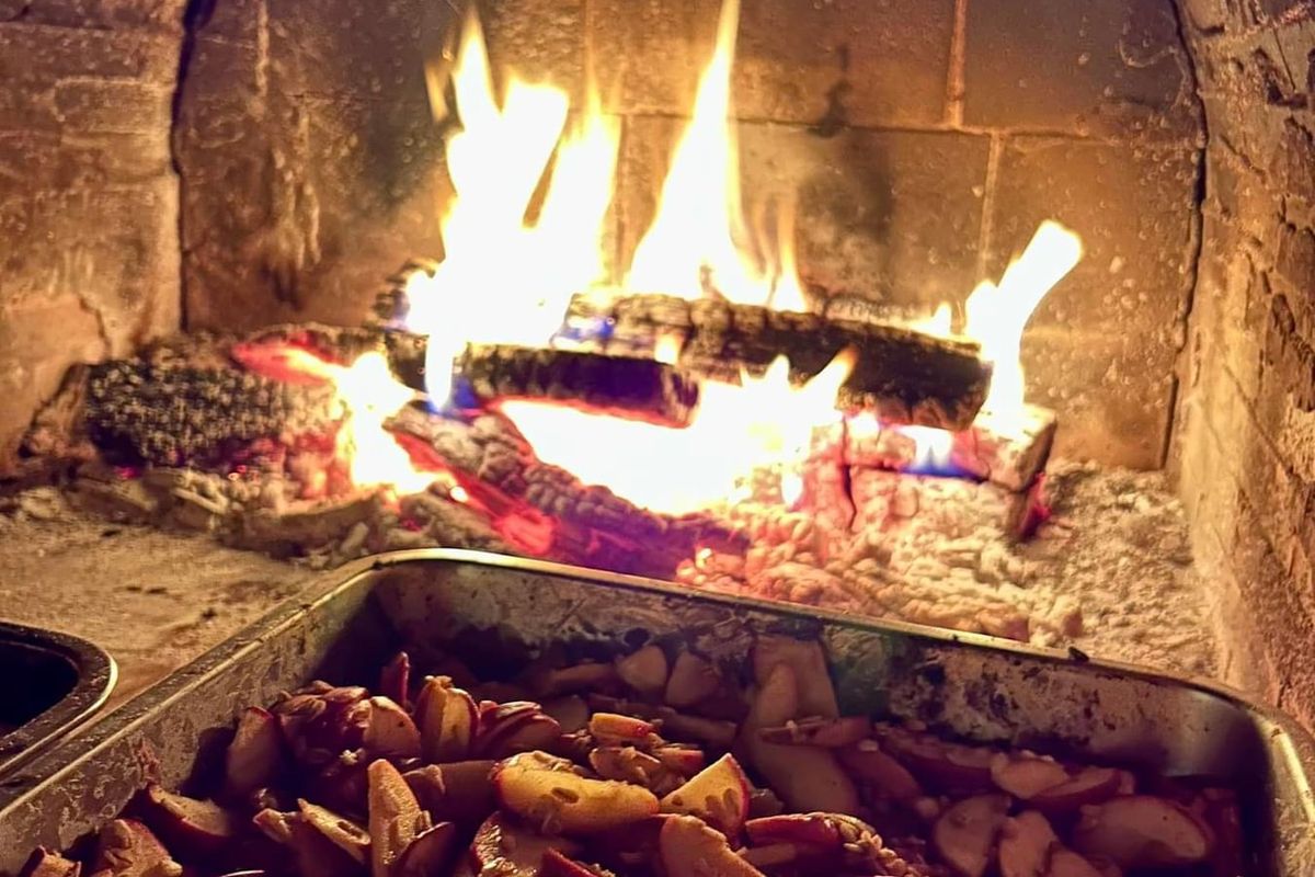 A tray of vegetables roasting in front of a wood fire in a brick oven