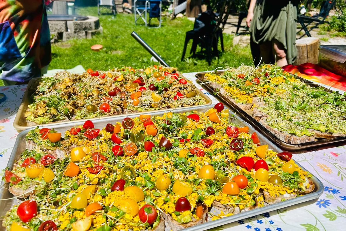Trays of flatbread topped with cherry tomatoes, sprouts and edible flowers at an outdoor gathering