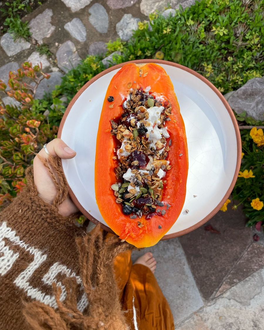 Half a papaya filled with granola, fruit and coconut, held over a garden path