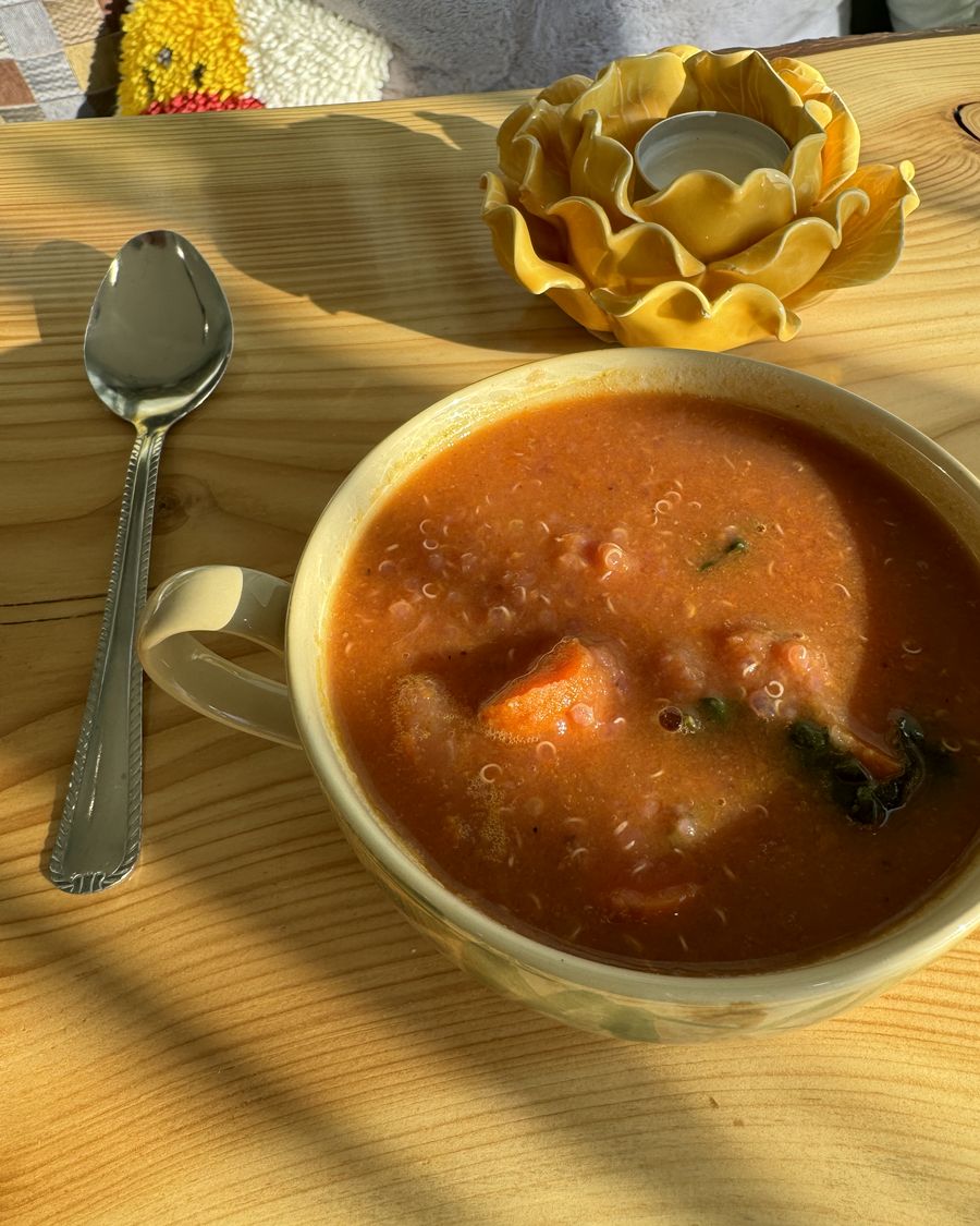 A mug of tomato and vegetable stew on a wooden table in the sun
